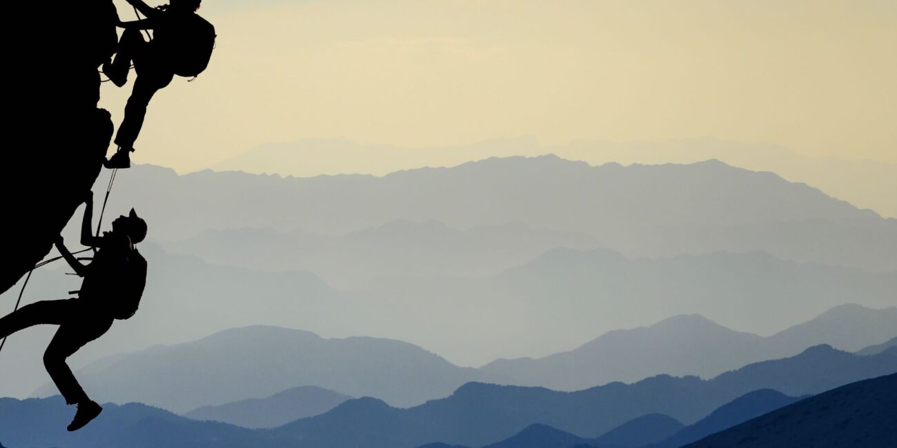 Two climbers climbing up a mountain side